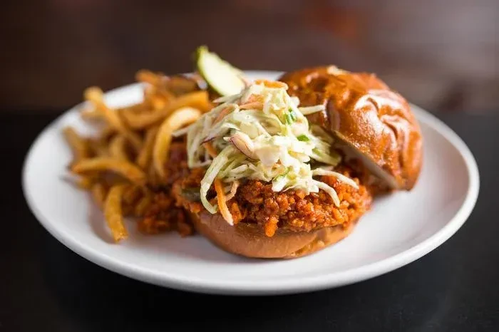 Sloppy joe sandwich with coleslaw, pickle, and curly fries.