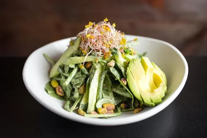 Green salad with sprouts, pistachios, and avocado in a white bowl.