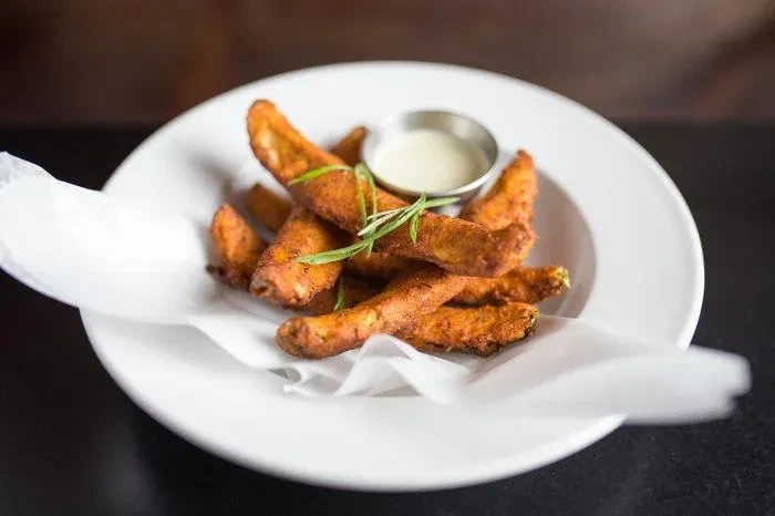 Fried potato wedges with creamy sauce and rosemary on a white plate.