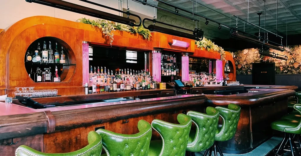 Stylish bar with dark wood, pink counter, and green bar stools.