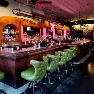 Dimly lit bar with liquor shelves, green stools, and decorations.