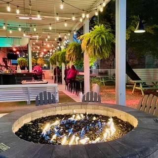 Outdoor restaurant patio with a circular fire pit and Adirondack chairs.
