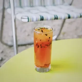 Orange drink with seeds on a green table by a beach chair.