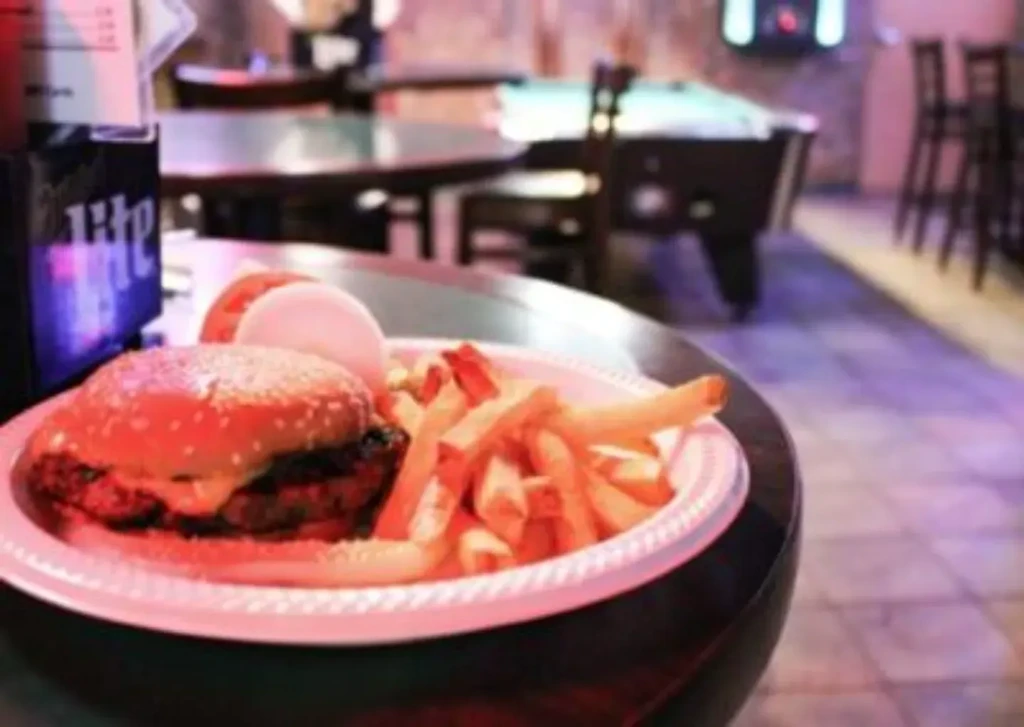 A blurry burger, fries, and a Miller Lite sign in a dim bar.