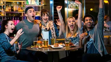 Five young adults watch a game in a lively bar.