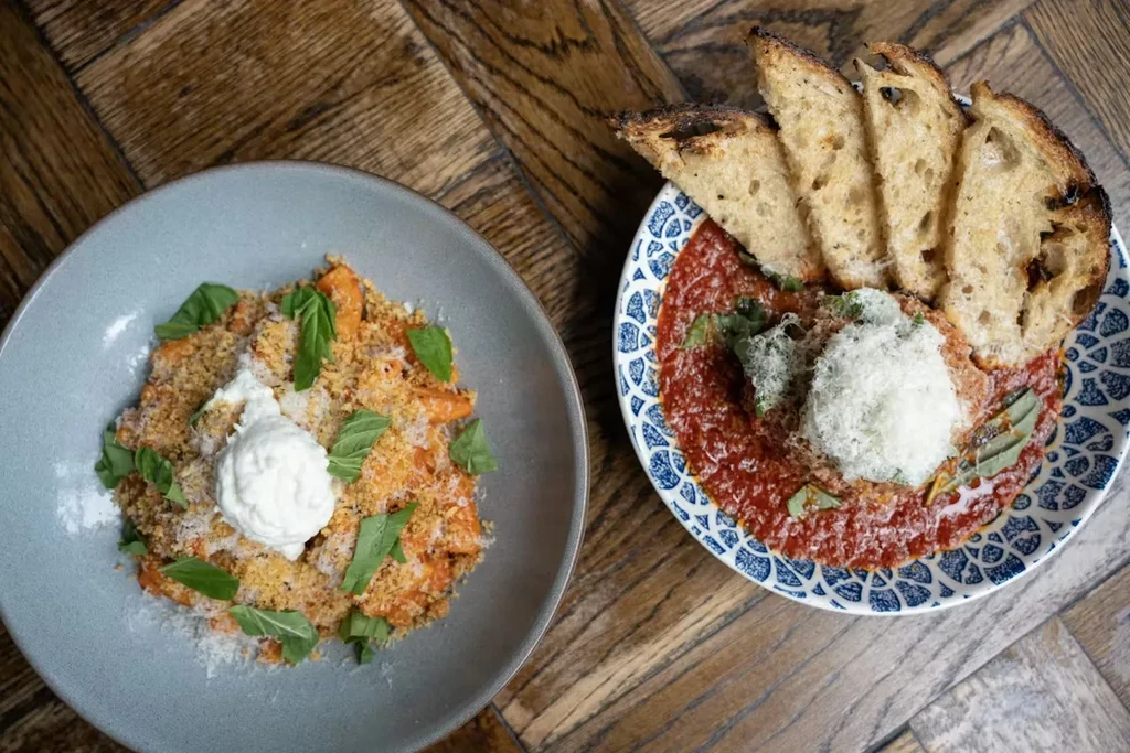 Two plates of pasta and tomato sauce on a wooden table.