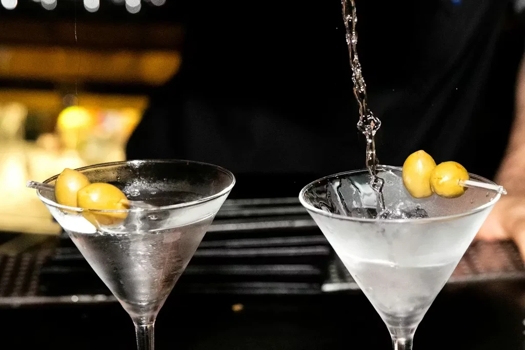 Two martini glasses, one being filled with a clear liquid.