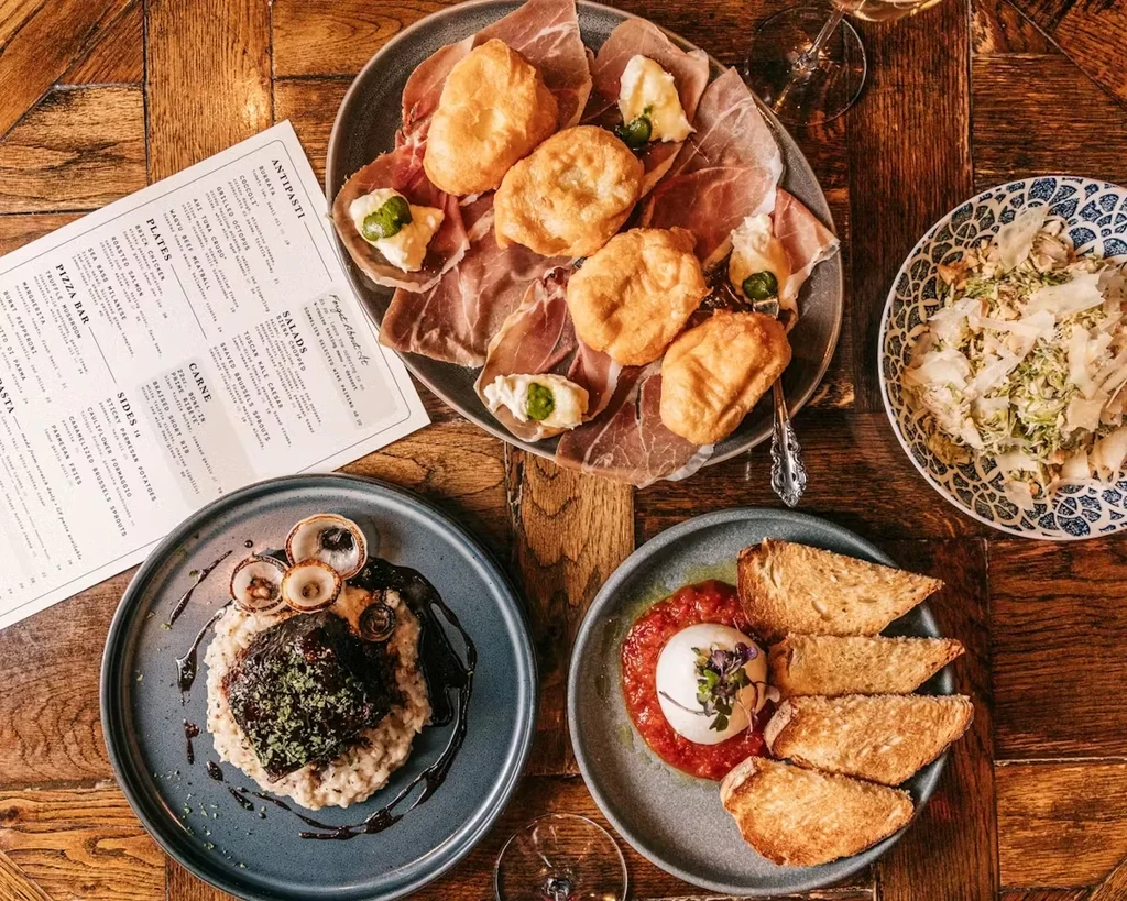 Overhead shot of charcuterie, salad, risotto, and burrata dishes on a table.