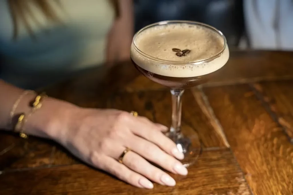 Espresso martini with coffee beans, woman's hand on a wooden table.