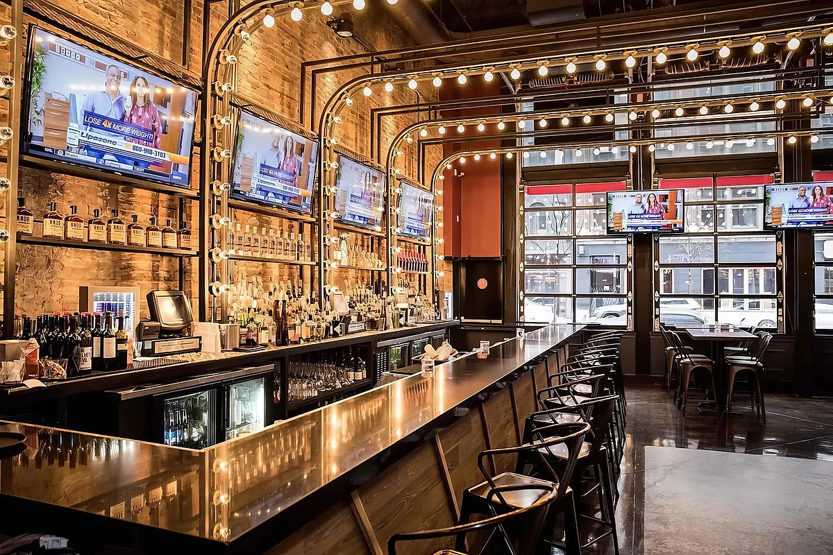 Long bar with exposed brick, string lights and wall-mounted TVs