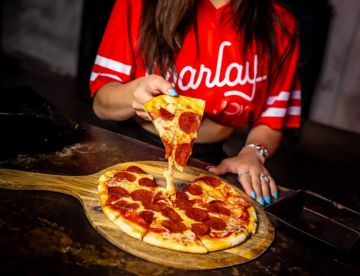 Pepperoni pizza on wooden board with slice being lifted