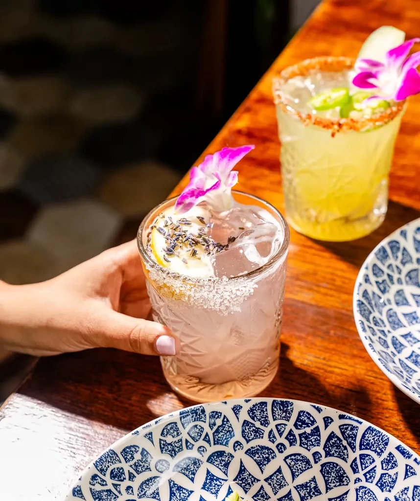 Two cocktails on a table, one purple, one yellow, both with orchids.
