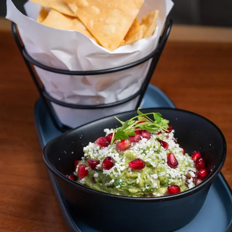 Guacamole topped with cheese and pomegranate, with tortilla chips.