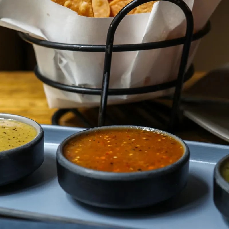 Three small bowls of dipping sauces and a basket of tortilla chips.