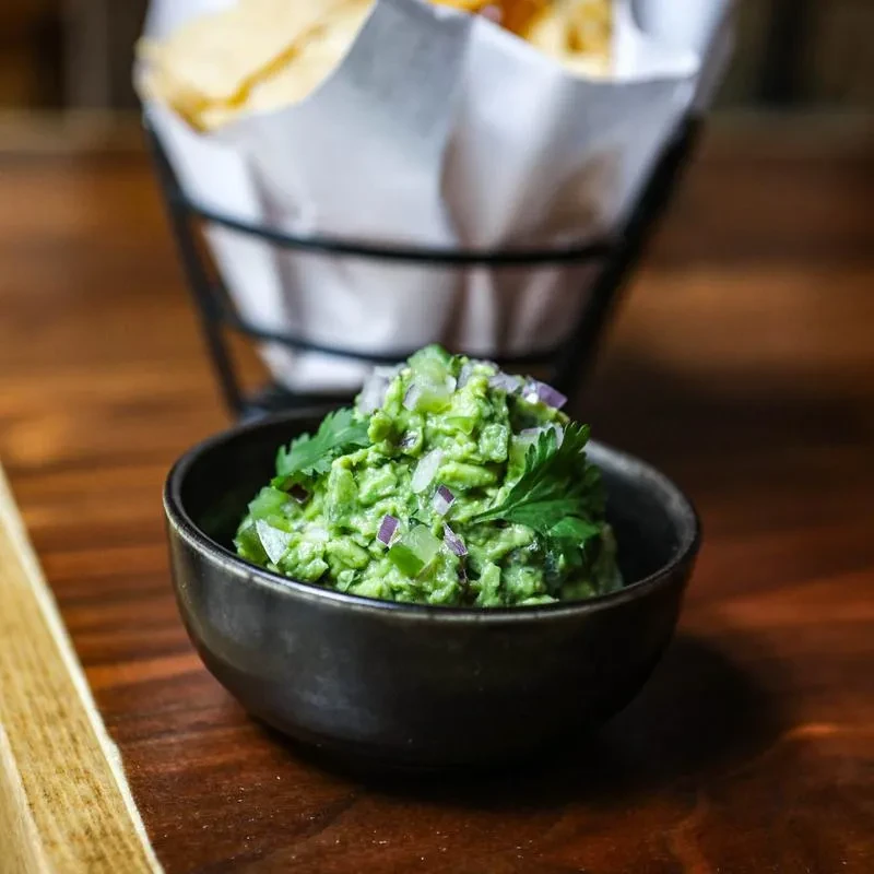 Close-up of a small bowl of guacamole on a wooden surface.