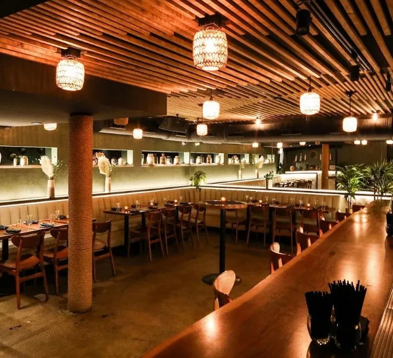 Restaurant interior with wooden bar, slat ceiling, and decorative lighting.