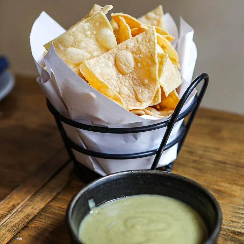 Golden-brown tortilla chips in a basket, with a creamy green dip.