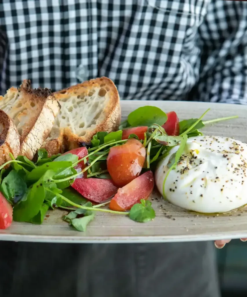 Close-up of toasted bread, salad, and burrata on a rustic plate.