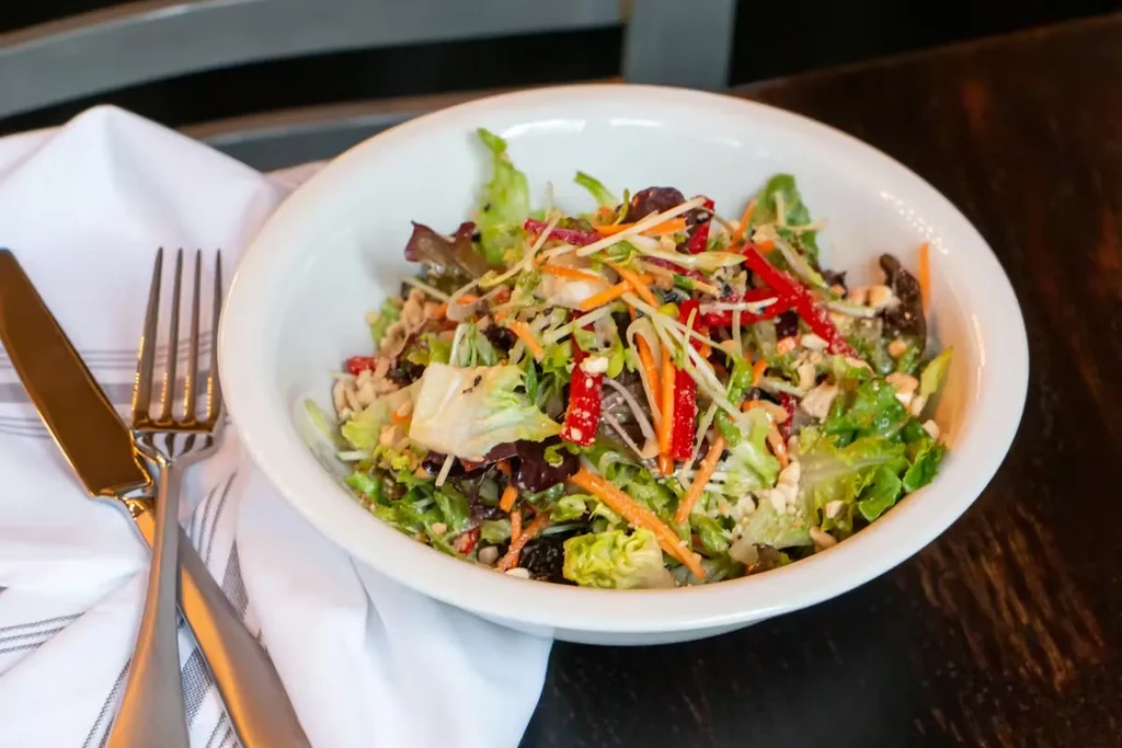 Vibrant salad in white bowl with fork and knife on wooden table.