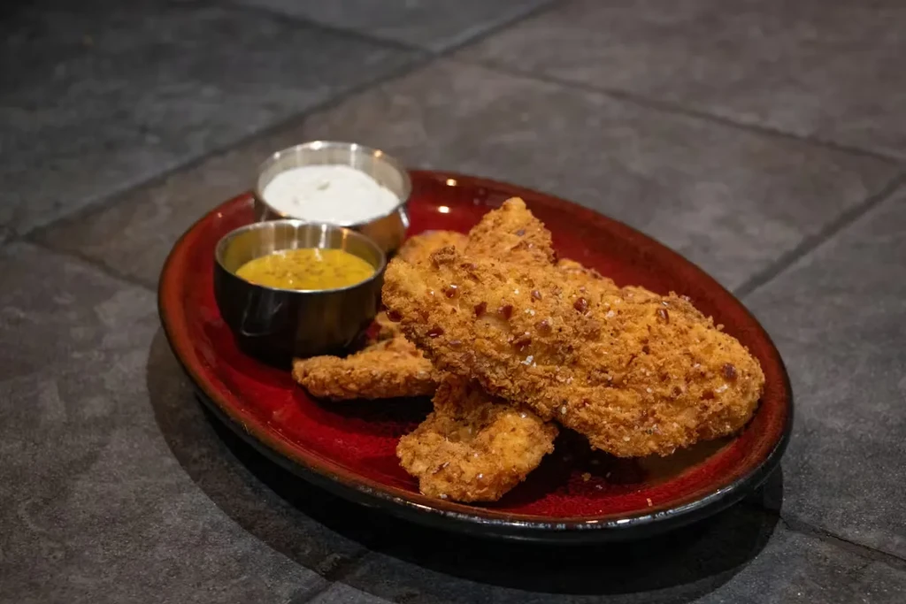 Crispy, breaded chicken tenders with white and yellow dipping sauces.