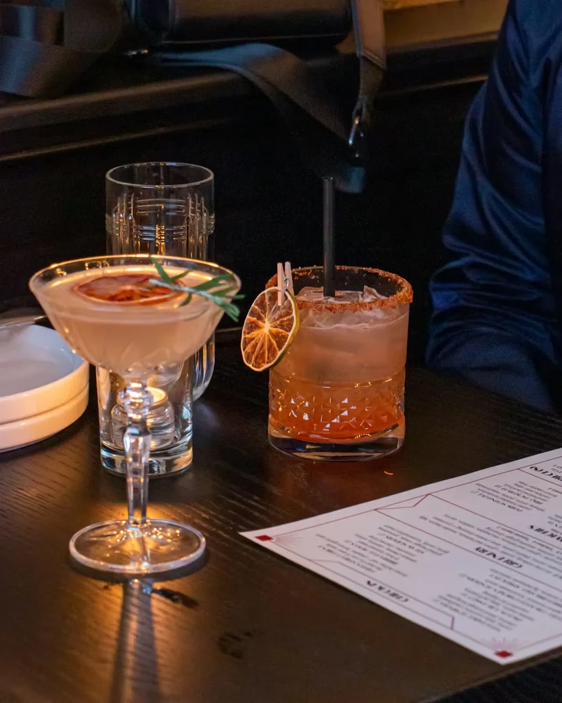 Two cocktails and a water glass on a dark wooden table.