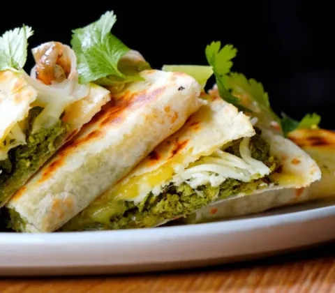 Close-up of triangular flatbread pieces with green filling and melted cheese.