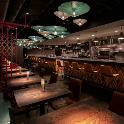 Modern restaurant interior with bar, dining tables, and open kitchen.