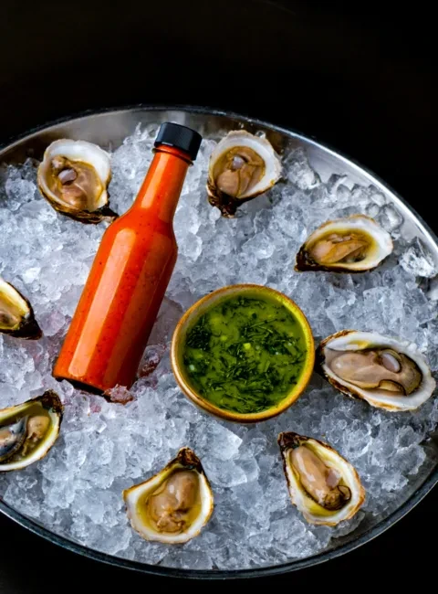 Freshly shucked oysters on ice with hot sauce and green sauce.