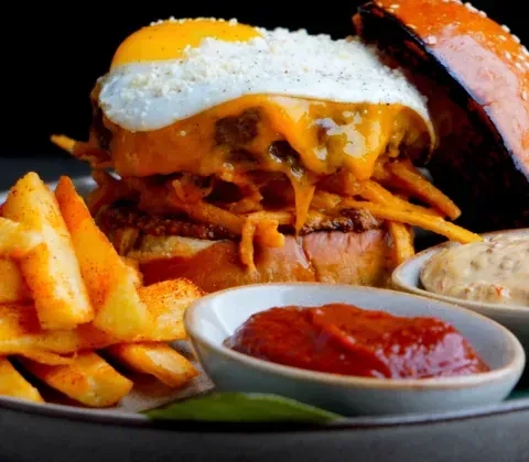 Gourmet burger with fried egg, fries, and two dipping sauces.