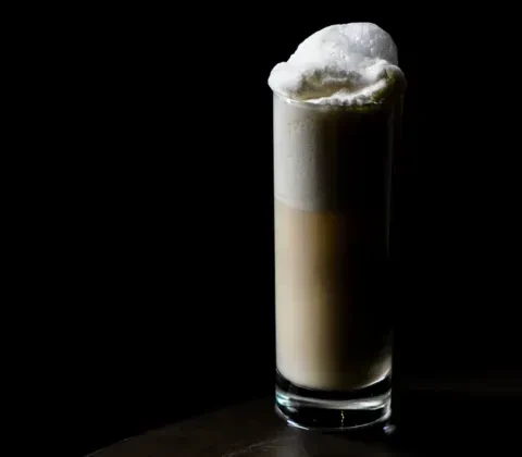 Glass of foamy light brown drink against a dark background.