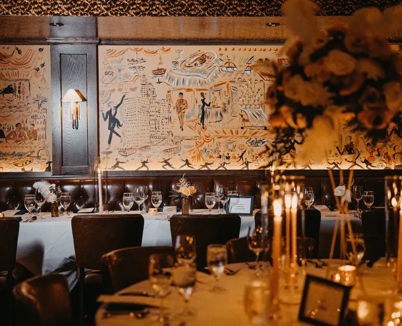 Restaurant interior with set tables, dark leather chairs, and wall murals.