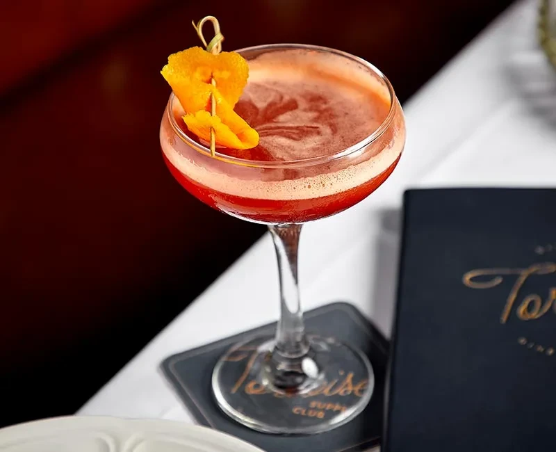 Cocktail in a coupe glass with an orange peel garnish.