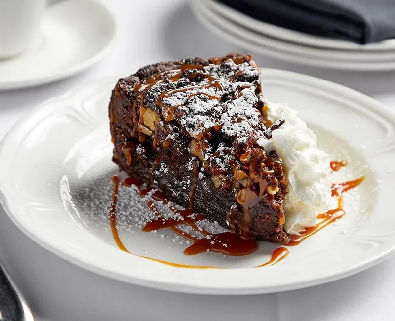 Chocolate cake with nuts, caramel, powdered sugar, and whipped cream.