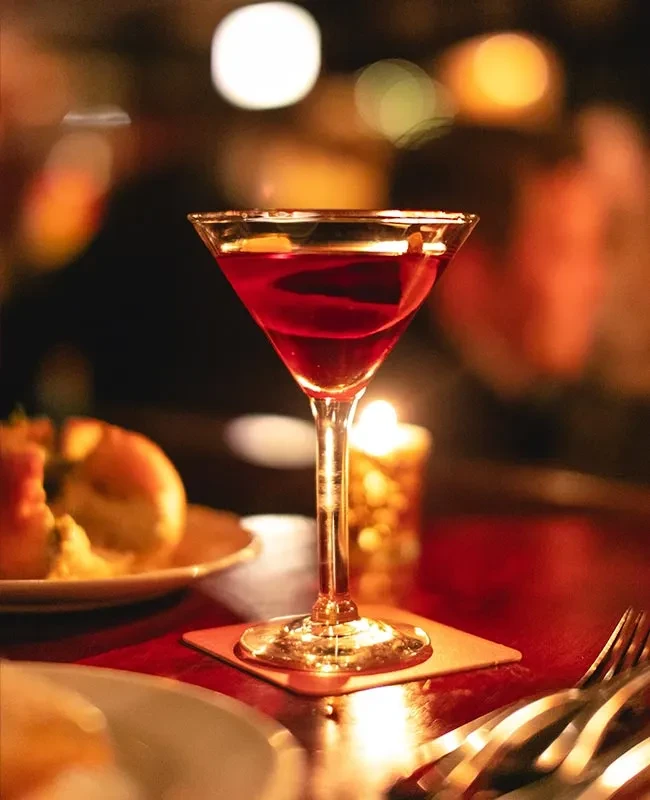 Crimson cocktail in a martini glass with a citrus peel garnish.