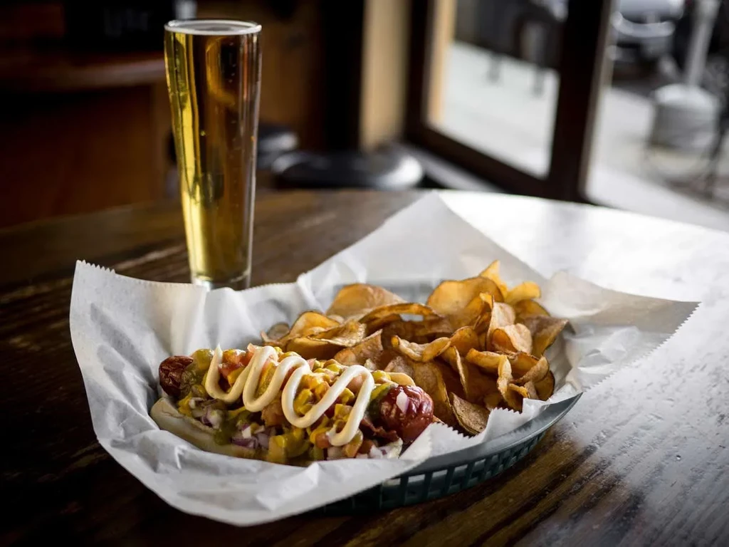 Hot dog with relish, onions, mustard, chips, and beer.