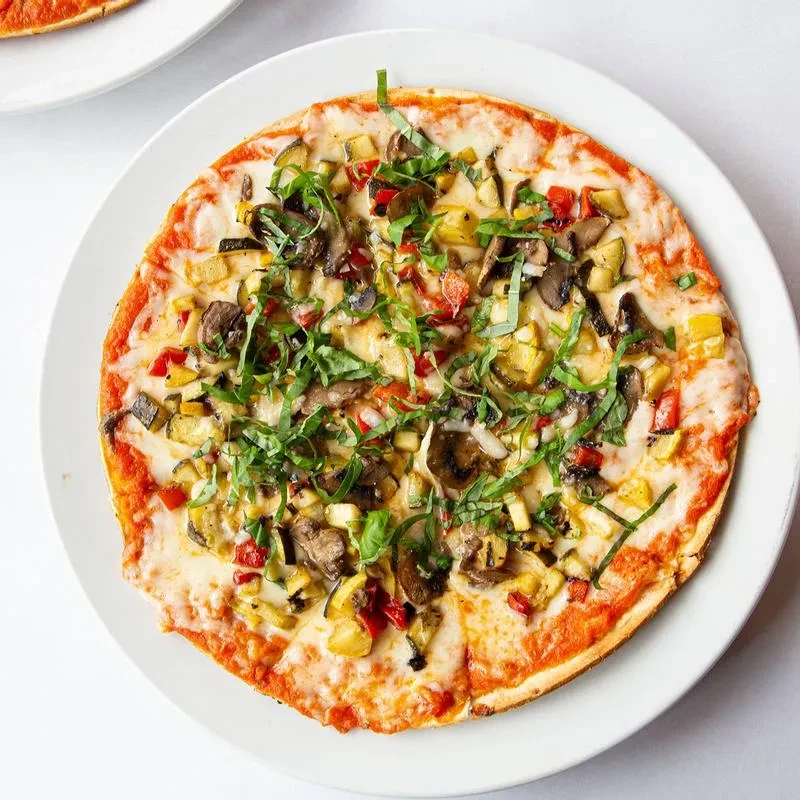 Thin-crust pizza with vegetables and herbs, viewed from above.