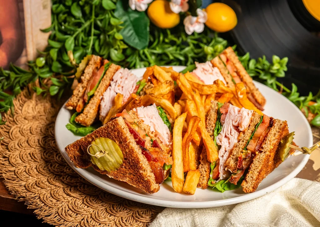 Club sandwich with fries, pickle, and lemon on a white plate.