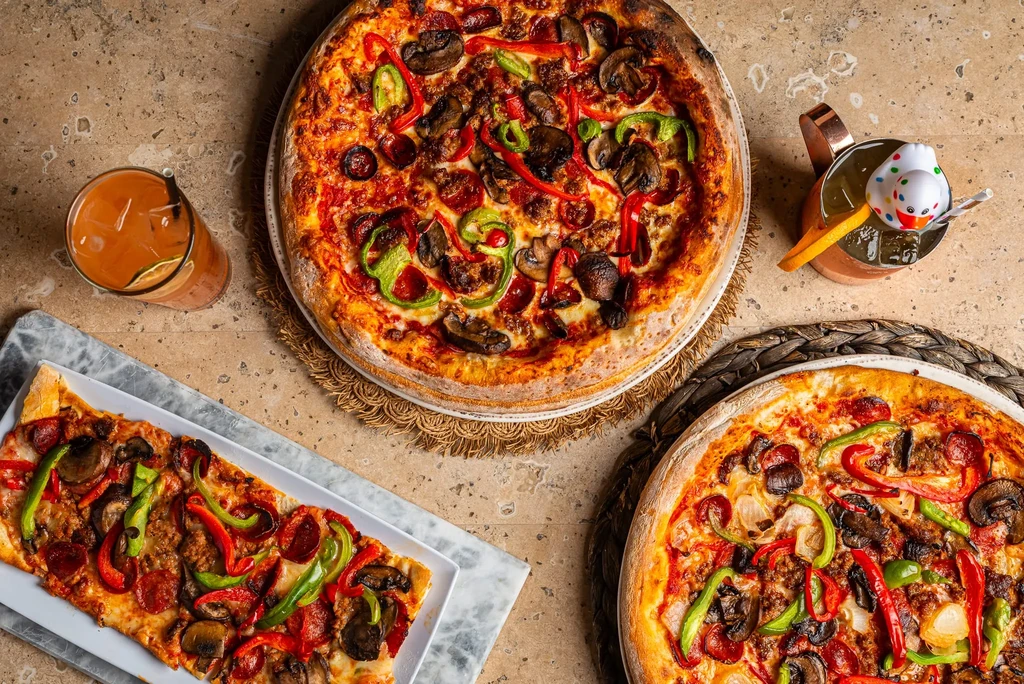 Overhead view of a table with three pizzas and two drinks.
