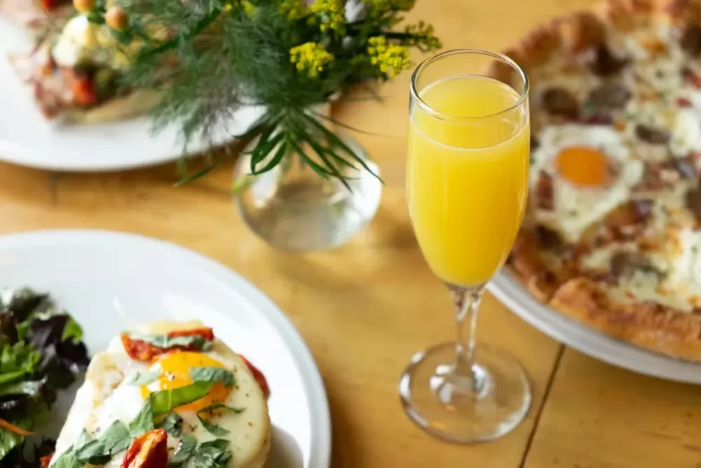 Fried egg, sun-dried tomatoes, salad, and mimosa on a wooden table.