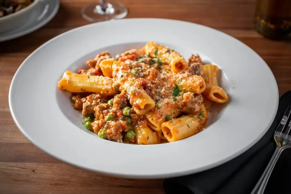 Rigatoni pasta with meat sauce, green peas, cheese, and herbs.