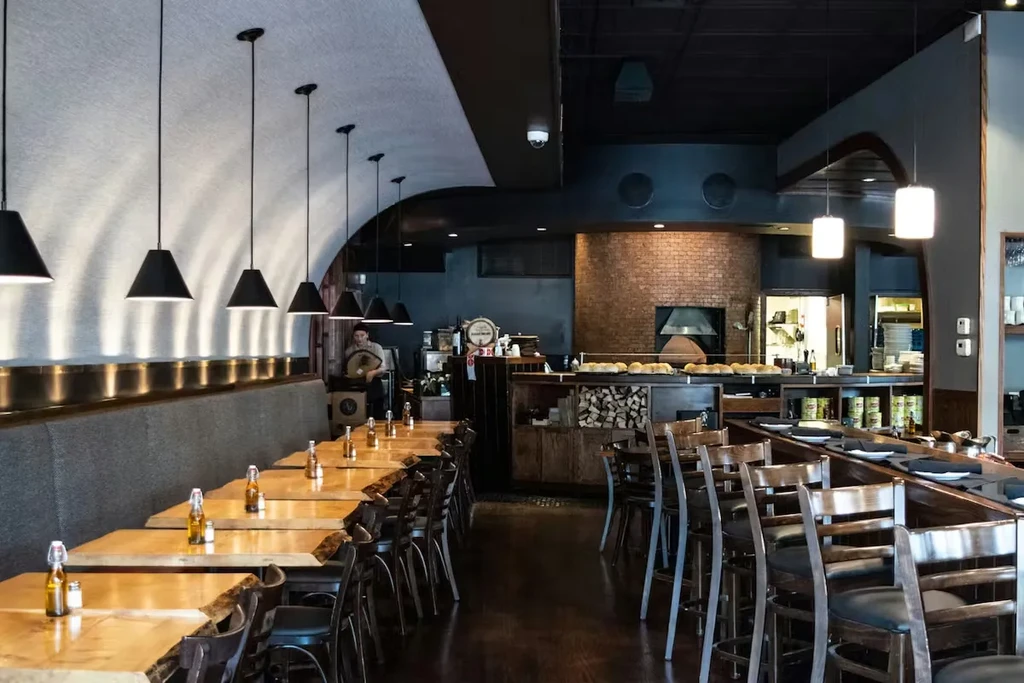 Restaurant interior with wooden tables, open kitchen, and brick oven.