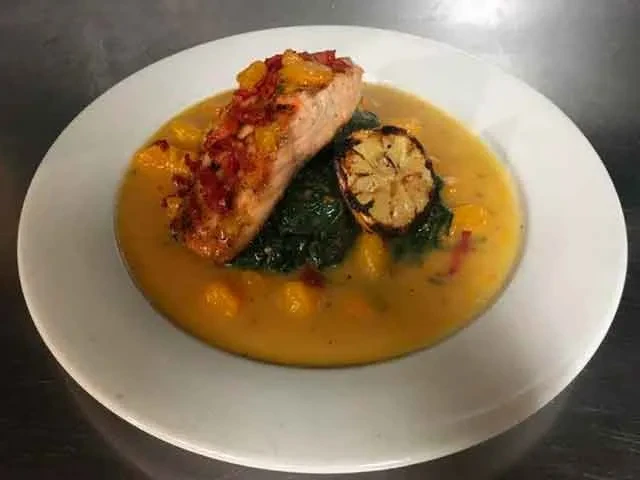 Plated salmon with relish, greens, charred lemon, and golden sauce.