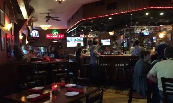 Dimly lit bar and dining room with customers, TVs, and Budweiser sign.