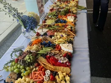 Overflowing long grazing table with cheeses, fruits, vegetables, and flowers.