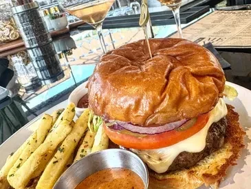 Gourmet burger, seasoned fries, dipping sauces, and wine on a table.