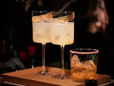 Three distinct sugary-rimmed cocktails with ice on a wooden tray.