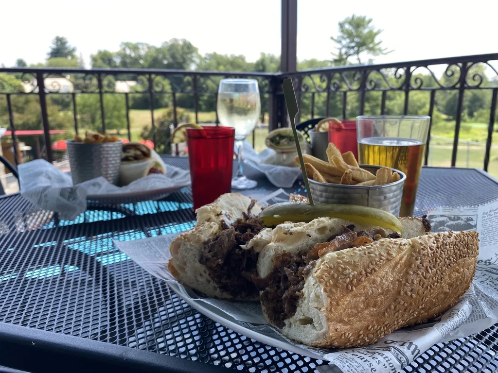 Outdoor dining with a hearty sandwich, fries, beer, and wine.