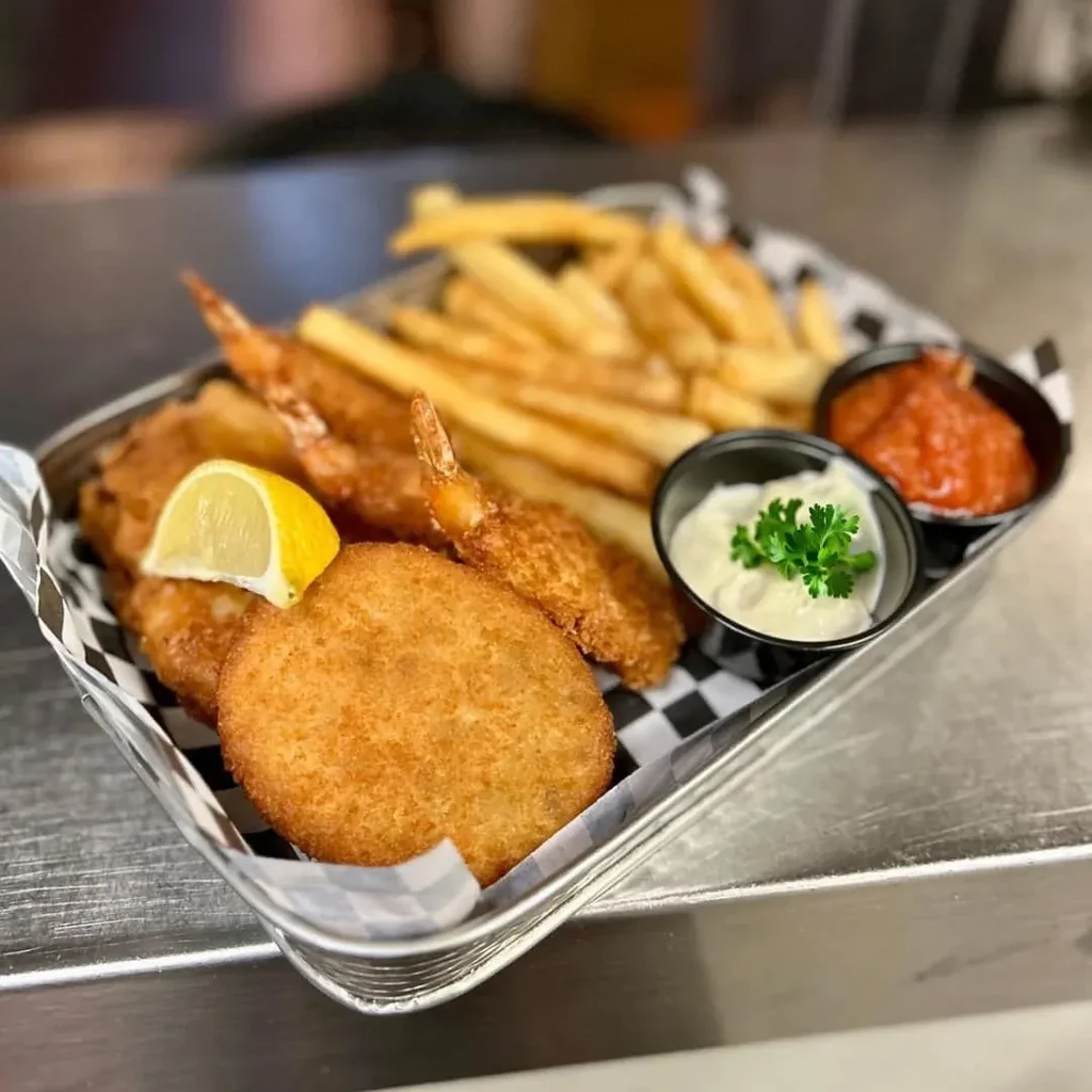Fried shrimp, fries, a fried patty, lemon, and two sauces in a basket.