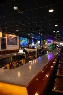 Dimly lit bar interior with a curved counter, stools, and colorful lights.