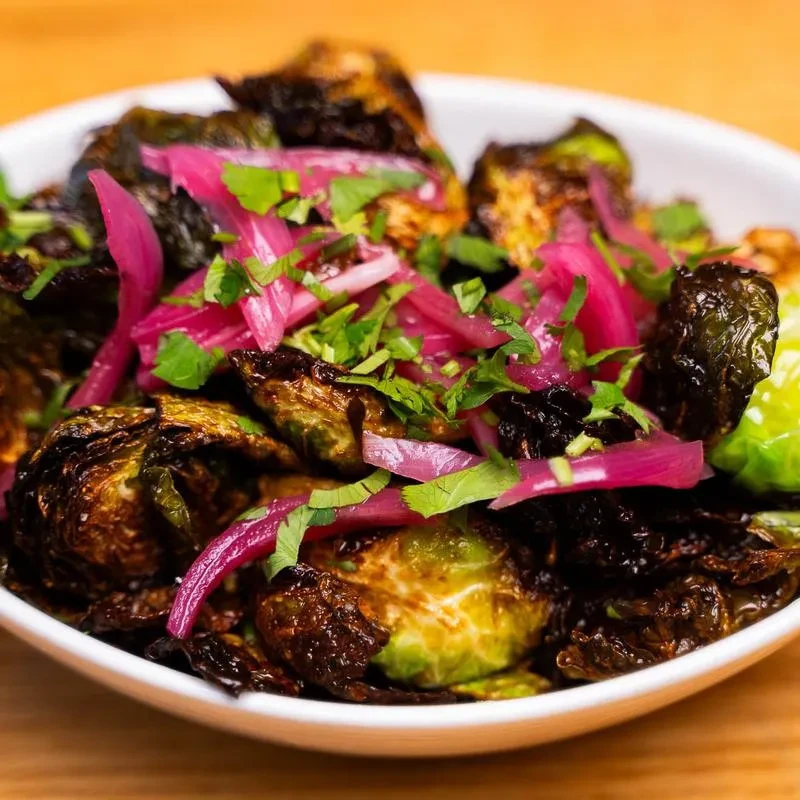 Roasted Brussels sprouts with charred edges, pink pickled onions, and green herbs.